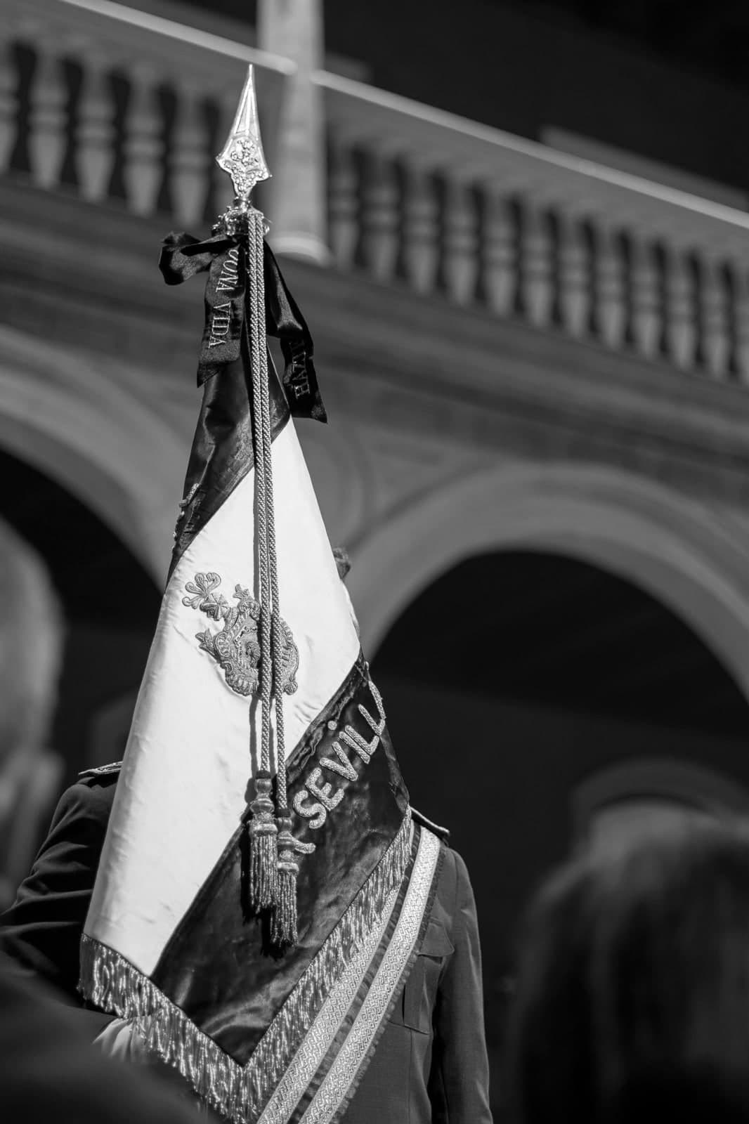 Banderín de la Agrupación con el escudo de Sevilla bordado y el lazo del Cristo de la Buena Muerte, en blanco y negro.